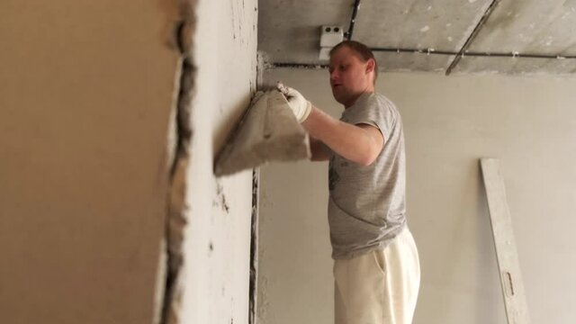 Male Builder Levels Plaster On Wall. Smooth Board. Removes Extra Layer. Renovation work in Residential Premises. Neat Movement. Profession. Thick Layer of Plaster. Preparing Walls for Whitewashing