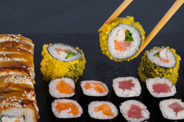 close-up, on a black table, assorted Japanese rolls of smoked eel, salmon and tuna