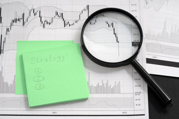 Financial instrument movement charts on white sheet of paper, magnifying glass on rebound chart, pen and sheets for notes lie on table. Preparing an entry strategy in a stock.