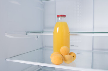 against the background of a white refrigerator, there is a bottle of juice and apricots on a glass shelf, close-up