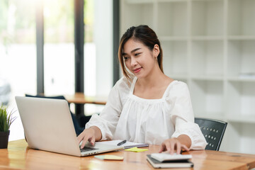 Portrait of smiling beautiful Asian businesswoman enjoy the idea sitting with laptop computer at office.