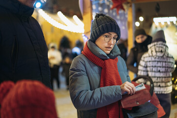 caucasian woman wearing hat and red scarf going to buy buying treats in kiosk with. Cash payment at christmas market