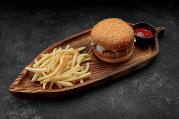 Burger with meat tomatoes and cheese, french fries and sauce, on a black background. Top view