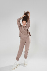 Young slim happy woman in a sports outfit pulling up her hair and posing on the white background
