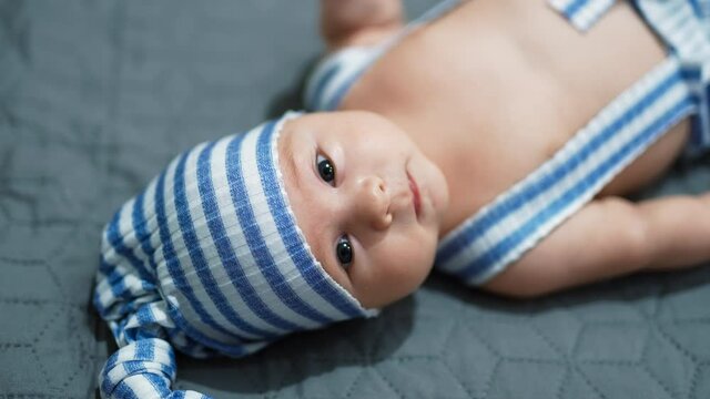 Toddler in a funny blue and white suit on the bed. Baby lies on the bed with his head to the camera. Close up.