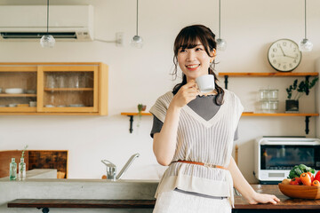 キッチンの前でホットドリンクを飲む女性
