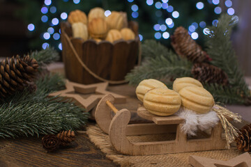 Nut-shaped cookies on a wooden sleigh. In the background there is a wooden cup with nuts, spruce branches with cones.