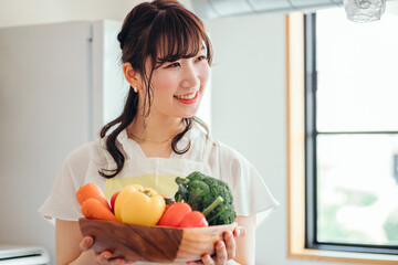 キッチンで野菜を持つ女性（笑顔）
