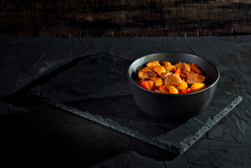 Yellow beans in a black bowl. Boiled beans with meat on a stone table. Beans with tomato sauce and pork. Contrasting dramatic light as an artistic effect.