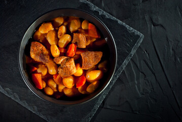 Yellow beans in a black bowl. Boiled beans with meat on a stone table. Beans with tomato sauce and pork. Contrasting dramatic light as an artistic effect.