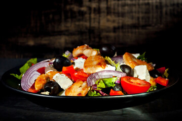 Salad with tomatoes, peppers, olives and chicken fillet. Fresh salad in a black plate on a dark background.