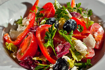 Salad with tomatoes, peppers, olives, cheese and cabbage. Fresh salad in a white plate on a light background.