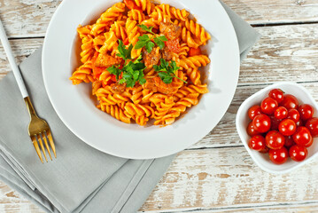 Pasta with meat and tomatoes in a white plate. Pasta on a shabby wooden table.