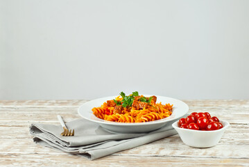 Pasta with meat and tomatoes in a white plate. Pasta on a shabby wooden table. Copy space and free space for text near food.