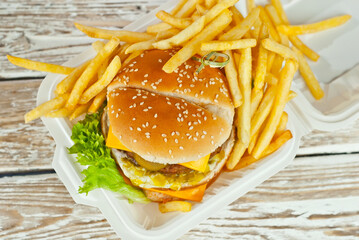 Cheeseburger in a white plate on an old shabby table. Burger and french fries close up. Food in an ecological container made from processed corn. Environmentally friendly dishes.