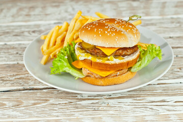 Cheeseburger in a white plate on an old shabby table. Burger and french fries close up. Food in an ecological container.