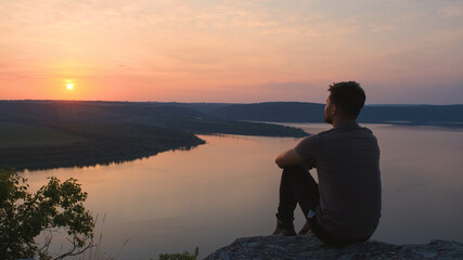 The young man sitting on rocky mountain above the beautiful river