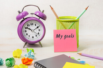 On the desk is an alarm clock, simple kandashi, a bookmarked notebook, crumpled paper, and a pink...