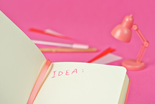 Notebook on a pink background. Toy table lamp near the notebook. Copy space and free space for text in notebook. Mockup for design. The word "idea" is written in pencil. Creativity concept.