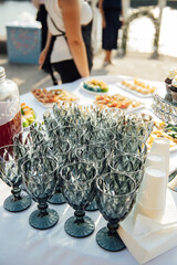 Elegant blue glasses without champagne stand in row next to canapes and snacks on picturesque background.