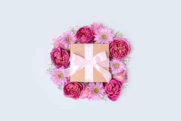 Gift box with a tied ribbon bow and flower frame. Present for springtime holidays on a blue pastel background.