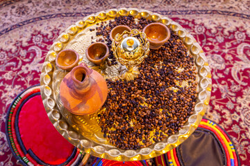 Caffe mocha coffee grains and arabic incenses on a golden tray with clay jugs and bowls, traditional Yemeni coffee table with colorful arabic majlis cushions.