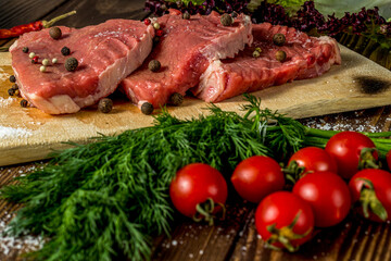 raw meat on a cutting board. beef steak with herbs, cherry tomatoes, onions