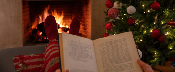 Christmas relaxation at home. Man with an open book, burning fireplace background.