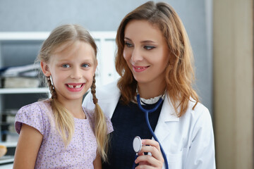 Smiling professional pediatrician posing with cute little girl on appointment