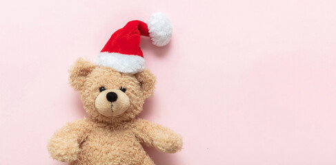 Christmas present. Teddy bear wearing Santa hat on pink background, Holiday greeting card.