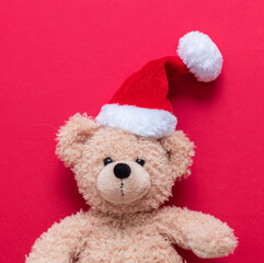 Christmas present. Teddy bear wearing Santa hat on red background, Holiday greeting card.
