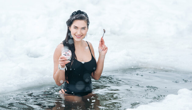 Girl with dessert in frozen lake ice hole. Woman hardening the body in cold water. Successful woman concept