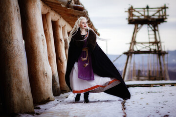 Beautiful blonde Viking dressed in a black cloak against the backdrop of the castle