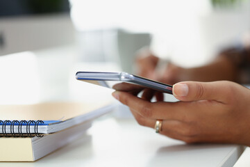 Naklejka premium Woman using modern smartphone while sitting at table with spiral notebook in office