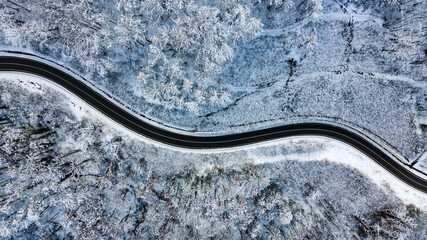 Top view of empty road along winter forest after snowfall. Aerial view of winding road through trees covered with snow