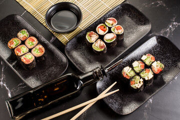 Fresh tasty sushi rolls with sticks and sauce on black background