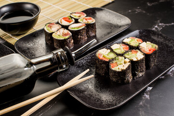 Fresh tasty sushi rolls with sticks and sauce on black background