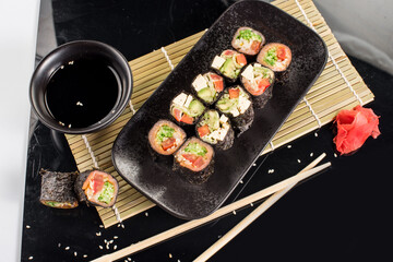 Fresh tasty sushi rolls with sticks and sauce on black background