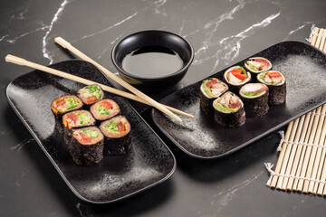 Fresh tasty sushi rolls with sticks and sauce on black background