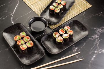 Fresh tasty sushi rolls with sticks and sauce on black background