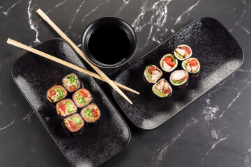 Fresh tasty sushi rolls with sticks and sauce on black background