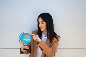 Young, beautiful woman holds a world ball in her hands and points to a country. The woman is a geography teacher. Concept of education and teaching. Travel and tourism