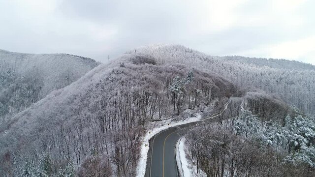 Aerial drone footage above winding road. Car driving in the winding road. Car driving on road in snowy forest. 겨울, 눈, 길, 도로, 자동차, 여행, 숲, 산