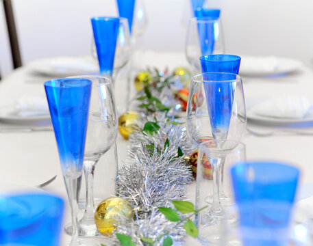A Christmas table in a long, unfocused foreground, with blue crystal glasses and red and gold Christmas balls with silver accents in the center of the table