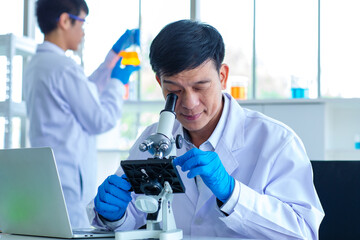 Asian professional mature male scientist in white lab coat and rubber gloves using microscope...