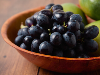 Dark grapes and fresh mango in a small wooden bowl and table. Still life. Light and rich saturated color. Agriculture product