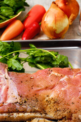 Raw uncooked pork belly on a stainless tray, herbs and veggie in the background. Meat industry product.