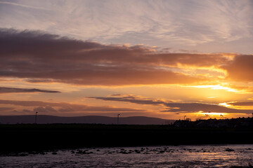 Stunning sunset sky over city houses silhouette. Rich warm orange color. Reflection in water surface.