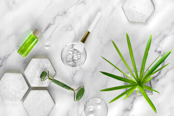 Fototapeta na wymiar Self made moisturizer and green jade face roller on marble hexagons. Exotic sedge water plant leaf on off white marble backdrop. Facial massage, handmade cosmetics.