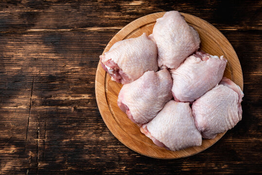 Raw chicken thighs on wooden board on dark wooden background.